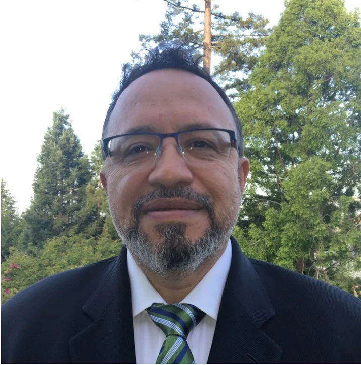 A man in a suit and glasses smiling.