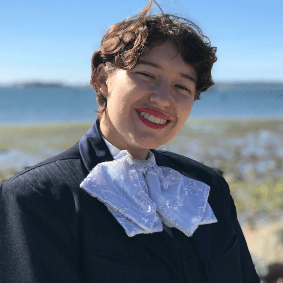 Smiling woman in a blue suit with a bow tie.