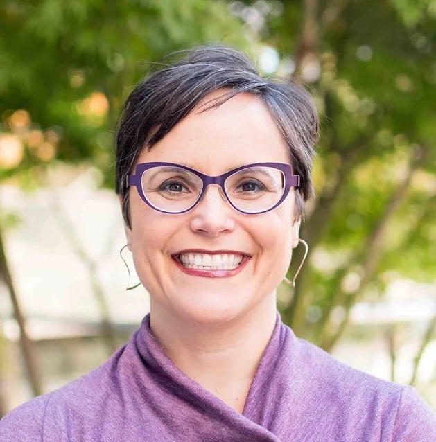 Smiling woman with glasses and purple shirt.